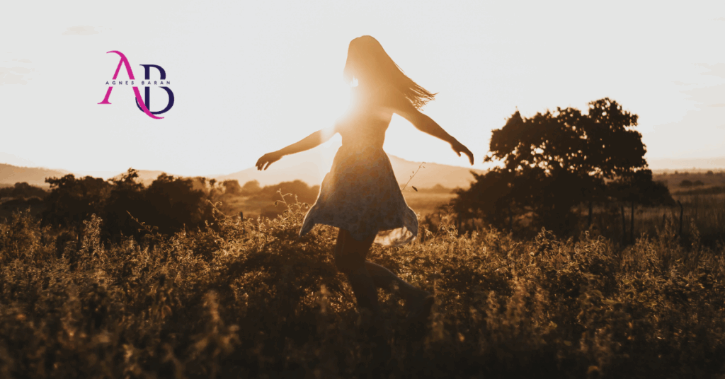 Kobieta tańcząca w promieniach słońca na tle natury – symbol nowego początku i wolności po zawodowym kryzysie