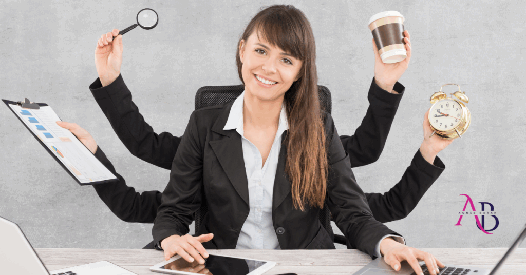 Kobieta w garniturze siedzi przy biurku, uśmiecha się, a jej cztery dodatkowe ręce trzymają lupę, kubek kawy, zegar i dokumenty, symbolizując lekkość w prowadzeniu biznesu spójnego z talentami Gallupa.